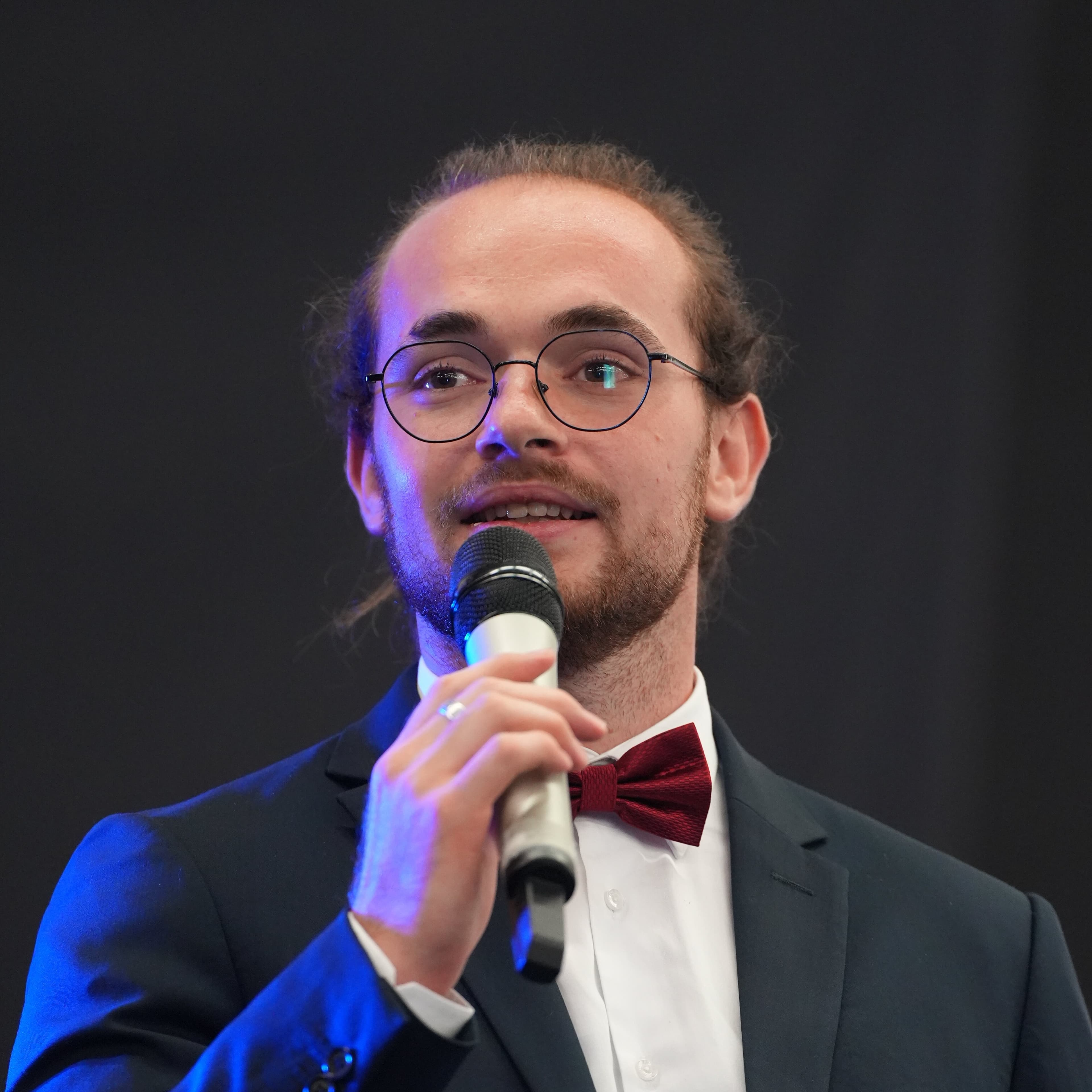 Portrait of Maxime Thoumin Desmullier, founder of CORAX.chat, in a suit, speaking into a microphone.